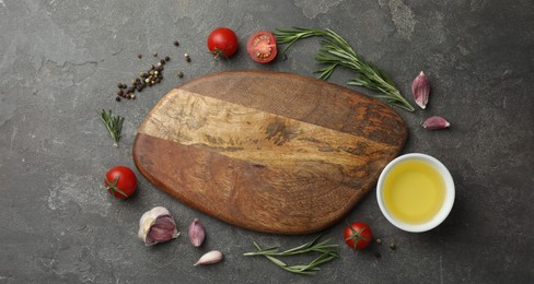 Photo of Cutting board, rosemary, garlic, oil and tomatoes on black table, flat lay. Space for text