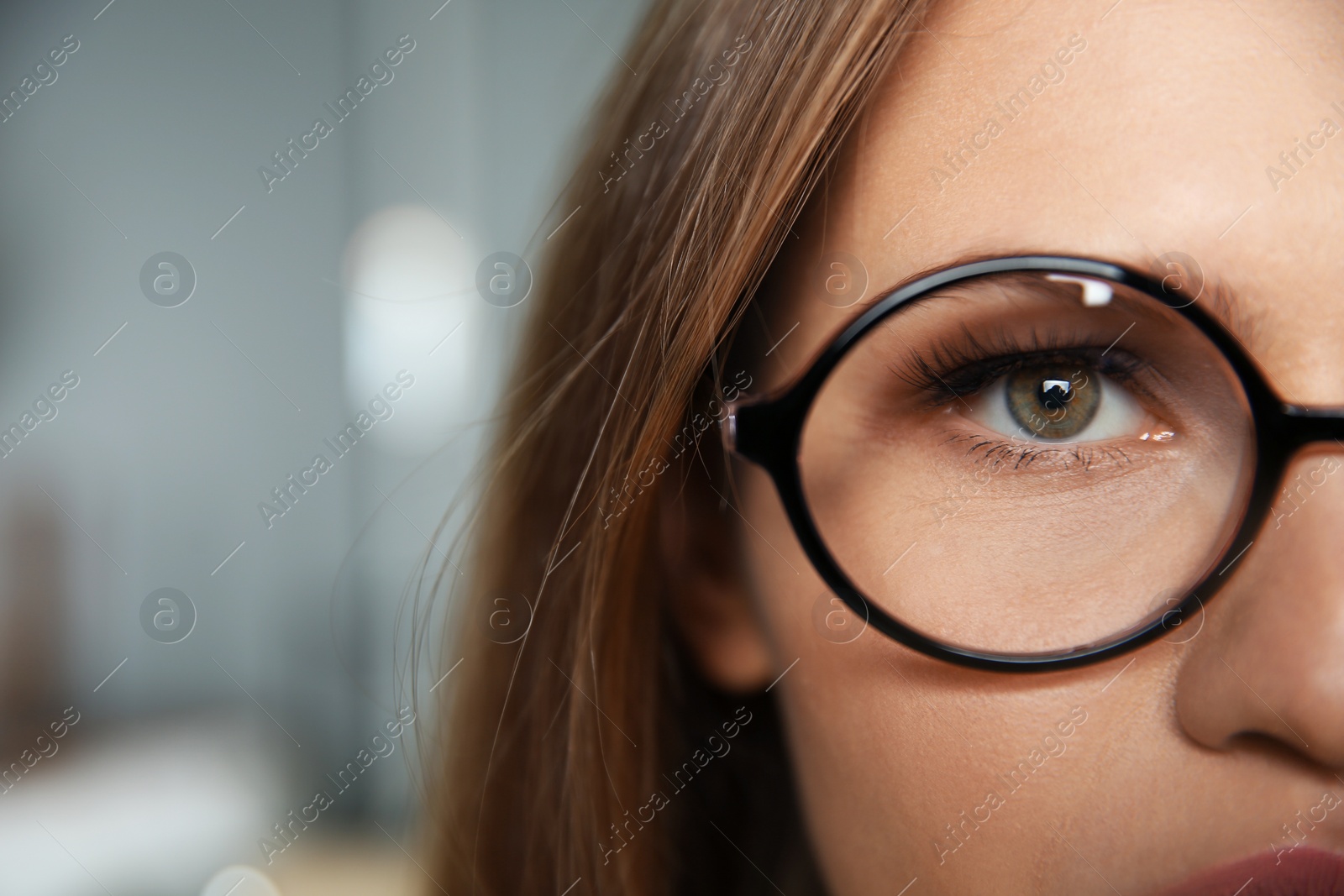 Photo of Young woman wearing glasses on blurred background, closeup. Ophthalmology service