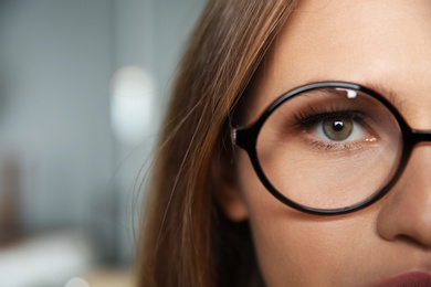 Photo of Young woman wearing glasses on blurred background, closeup. Ophthalmology service