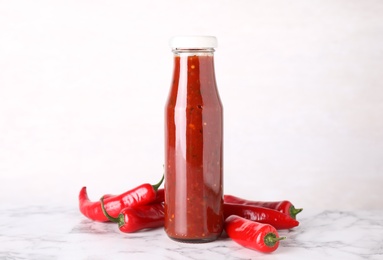 Photo of Glass bottle of hot chili sauce with peppers on table