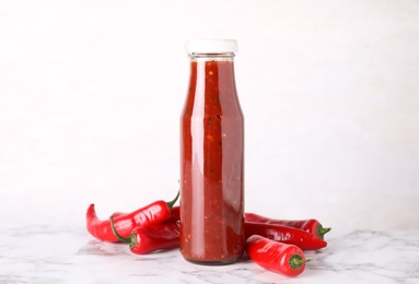 Glass bottle of hot chili sauce with peppers on table