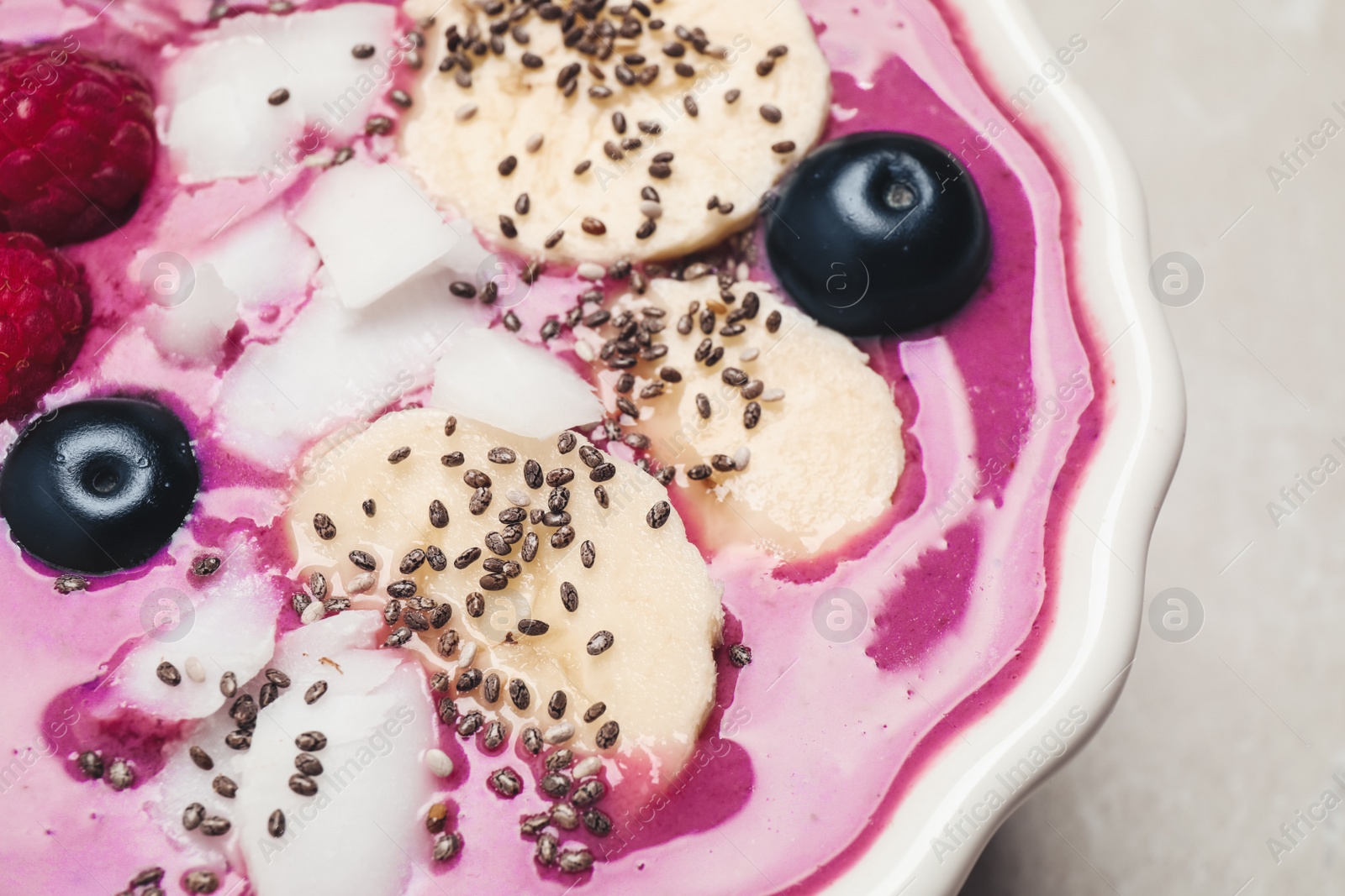 Photo of Delicious acai smoothie with fruits and coconut chips on grey table, closeup