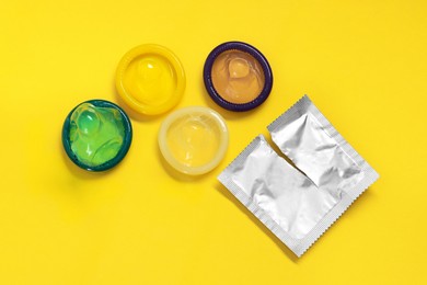 Photo of Unpacked condoms and package on yellow background, flat lay. Safe sex