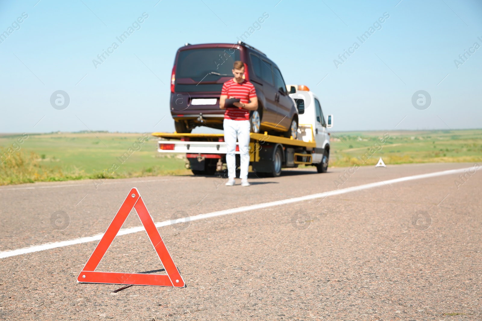 Photo of Emergency stop sign and man near tow truck with broken car on background