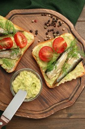 Photo of Delicious sandwiches with sprats, tomatoes, dill and avocado puree served on wooden table, top view