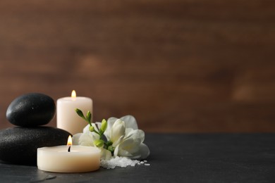 Photo of Beautiful composition with spa stones, burning candles and flowers on black table. Space for text