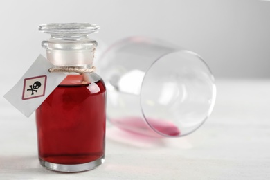 Photo of Bottle of poison and partially emptied glass on light background, closeup. Space for text