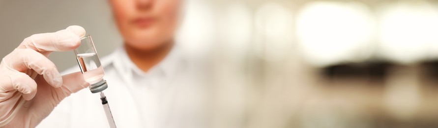 Image of Doctor filling syringe with medication from glass vial on blurred background, closeup. Banner design