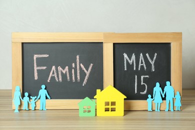 Photo of Happy Family Day. Blackboards, paper parents and their children near house models on wooden table
