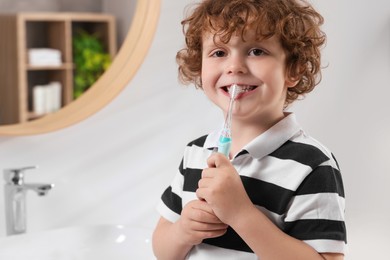 Photo of Cute little boy brushing his teeth with electric toothbrush in bathroom, space for text
