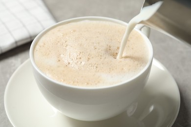 Pouring milk into cup of coffee on grey table, closeup