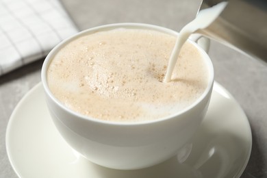 Photo of Pouring milk into cup of coffee on grey table, closeup