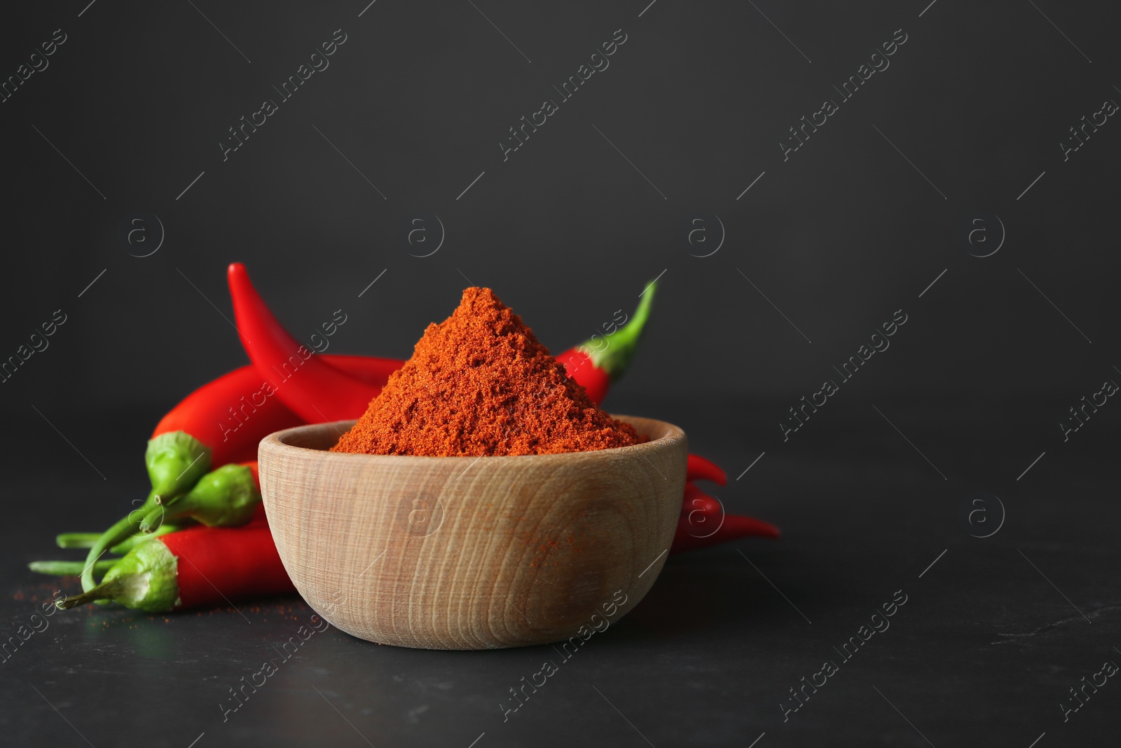 Photo of Paprika powder and fresh chili peppers on black table. Space for text