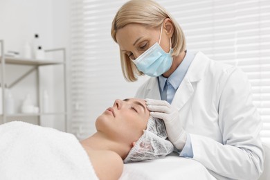 Dermatologist in medical mask examining patient`s face in clinic