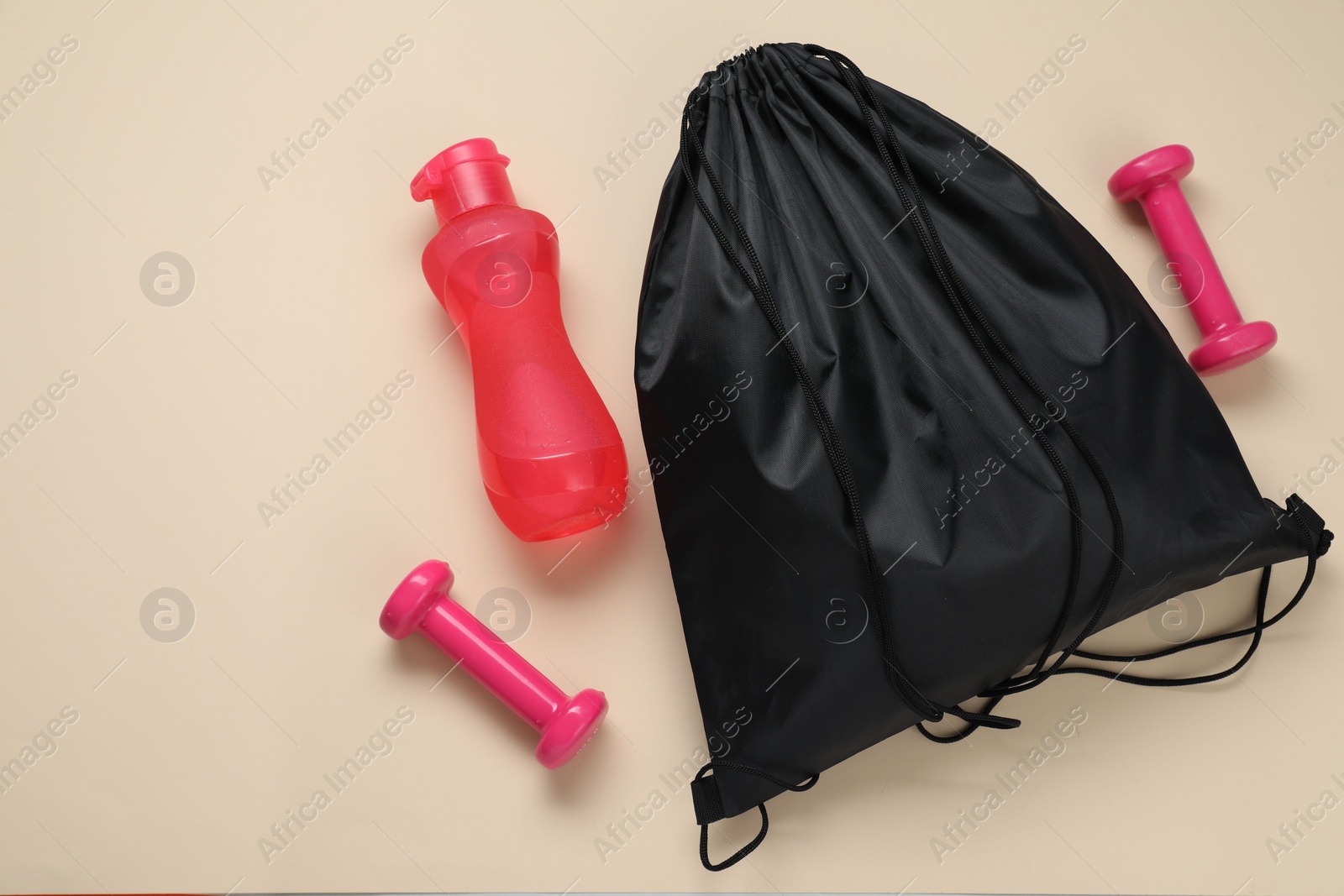 Photo of Black drawstring bag, bottle and dumbbells on beige background, flat lay. Space for text