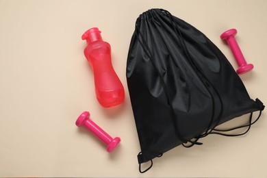 Photo of Black drawstring bag, bottle and dumbbells on beige background, flat lay. Space for text