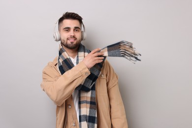 Smiling man in warm scarf listening to music on light grey background