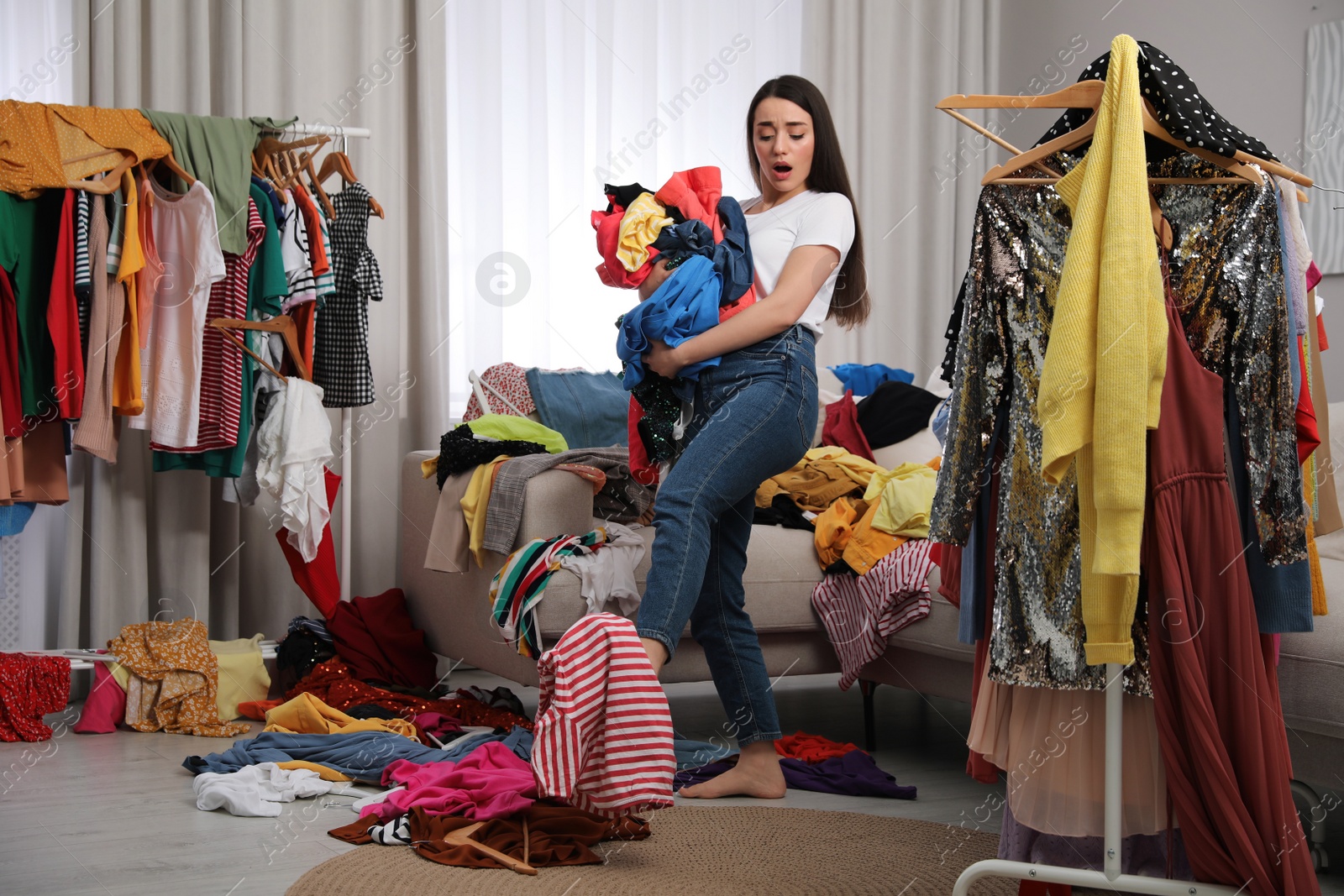 Photo of Upset young woman with lots of clothes in room. Fast fashion