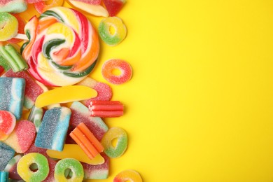 Photo of Many different jelly candies and lollipop on yellow background, flat lay. Space for text