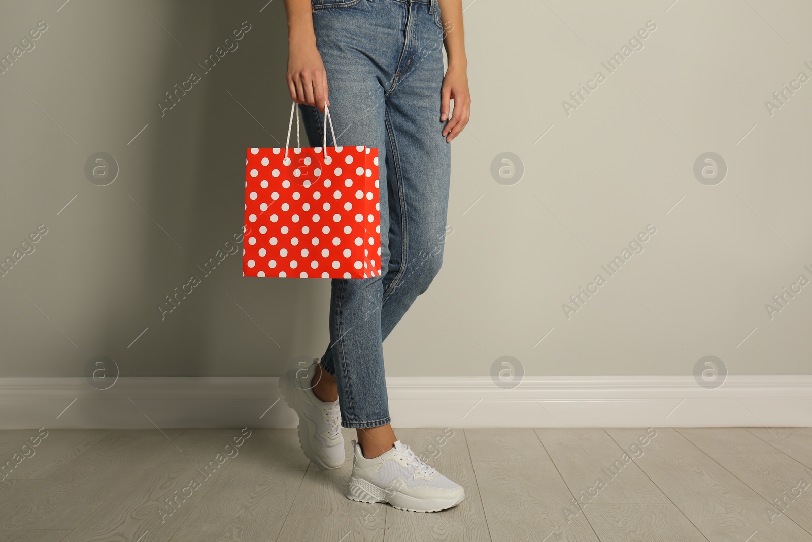 Photo of Woman with paper shopping bag near light grey wall, closeup