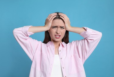 Young woman suffering from headache on light blue background