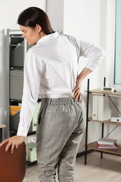 Photo of Young woman suffering from back pain in office. Symptom of scoliosis