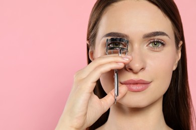 Photo of Woman using eyelash curler on pink background, space for text