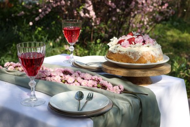 Beautiful spring flowers, delicious cake and wine glasses on table in garden