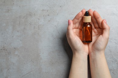 Woman holding bottle with serum at grey table, top view. Space for text