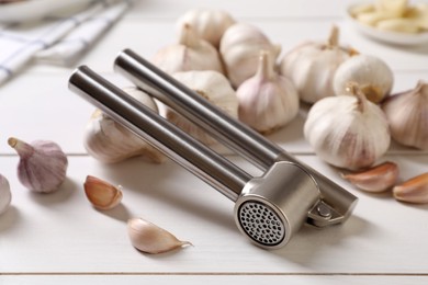 Photo of Metal press and garlic on white wooden table, closeup