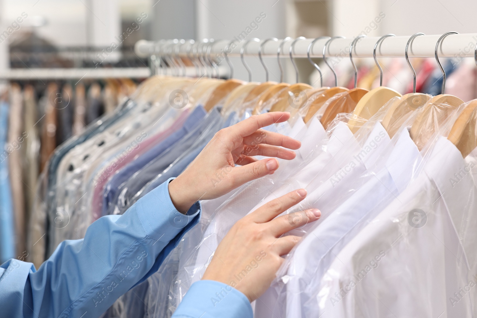 Photo of Dry-cleaning service. Woman taking shirt in plastic bag from rack indoors, closeup