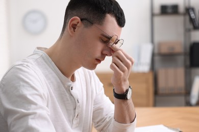 Photo of Young man suffering from headache in office, space for text