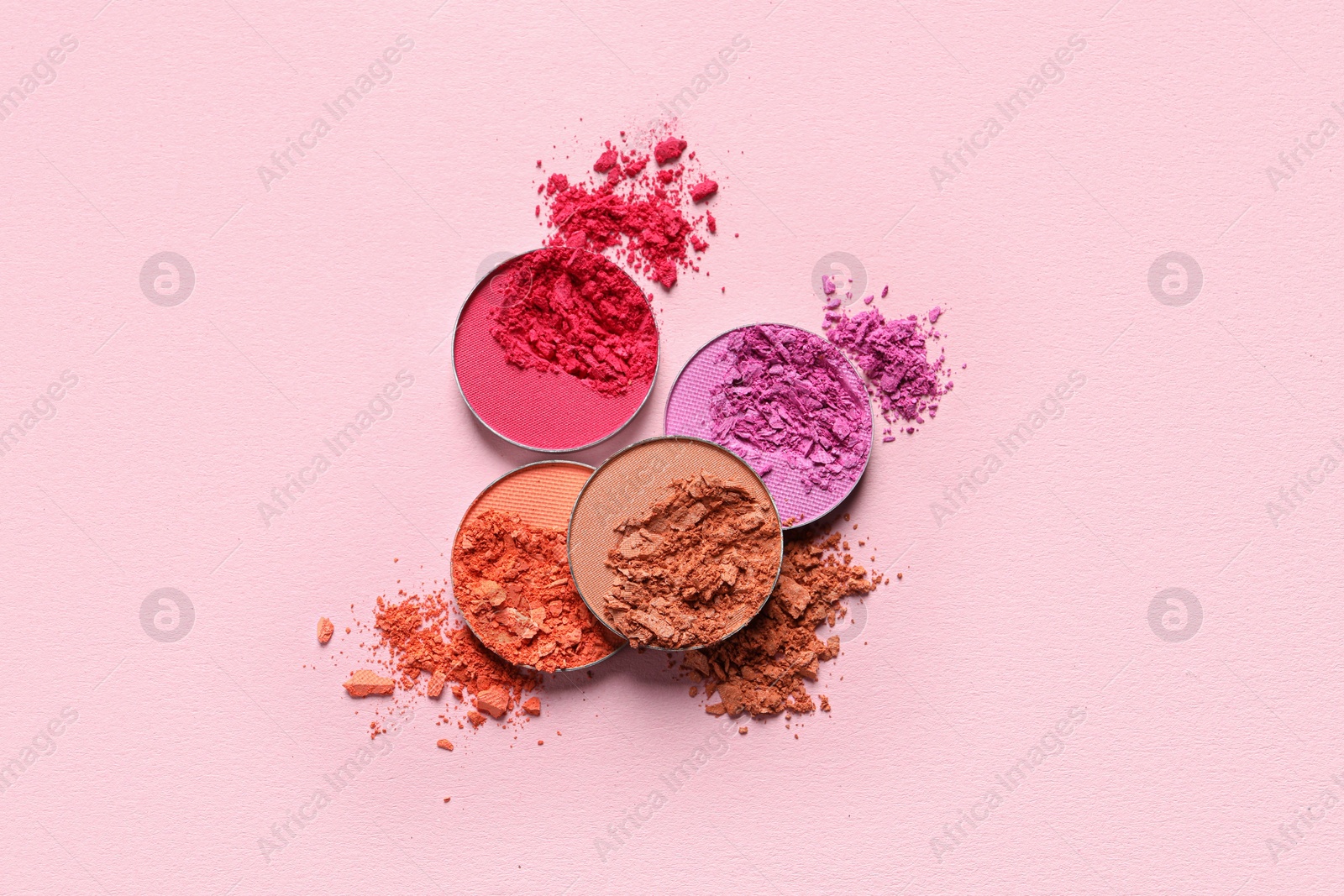 Photo of Different crushed eye shadows on pink background, flat lay