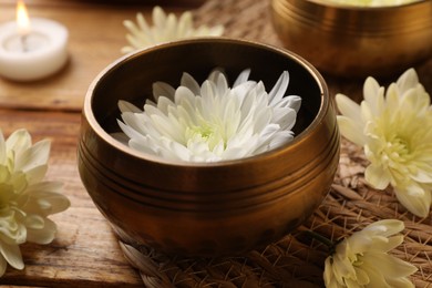 Tibetan singing bowl and beautiful chrysanthemum flowers on wooden table, closeup