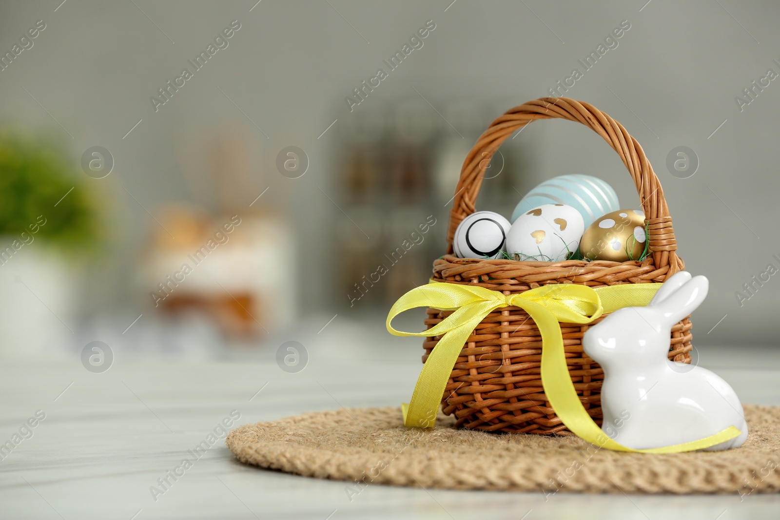 Photo of Small Easter basket with painted eggs near rabbit figure on white marble table. Space for text