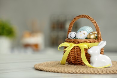Photo of Small Easter basket with painted eggs near rabbit figure on white marble table. Space for text