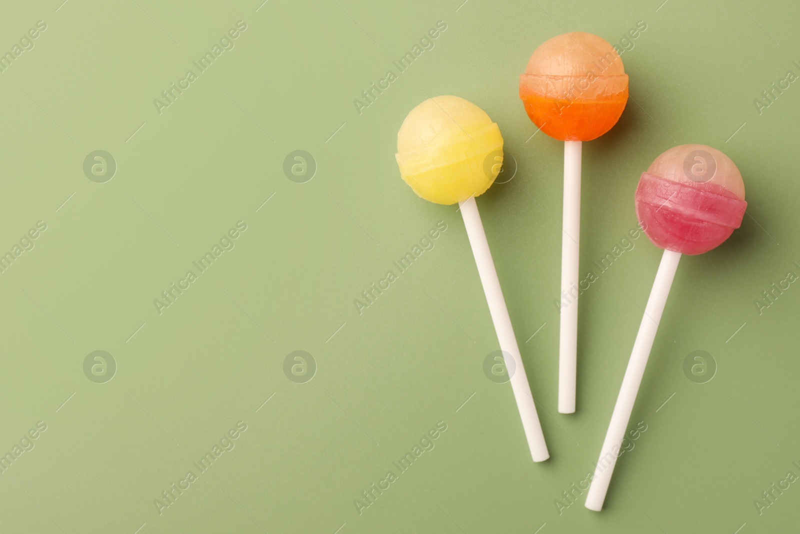 Photo of Tasty lollipops on green background, flat lay. Space for text