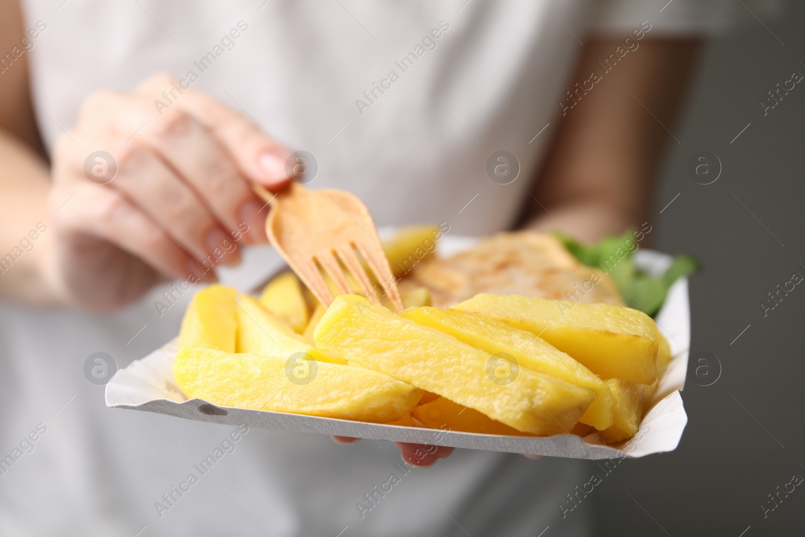 Photo of Woman eating delicious fish and chips on gray background, closeup