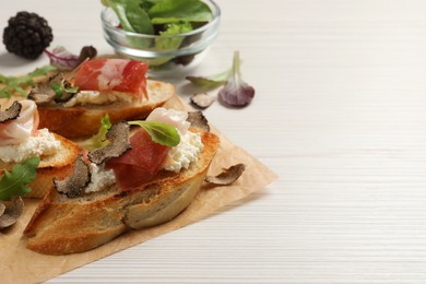 Photo of Delicious bruschettas with cheese, prosciutto and slices of black truffle on white wooden table. Space for text