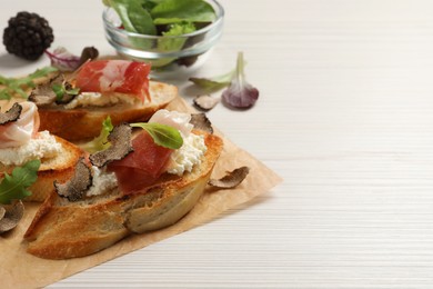 Delicious bruschettas with cheese, prosciutto and slices of black truffle on white wooden table. Space for text