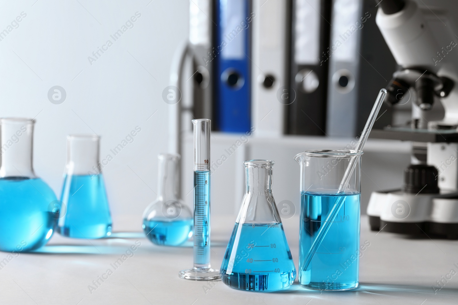 Photo of Different laboratory glassware with light blue liquid on table