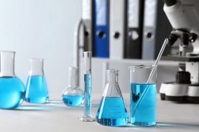 Photo of Different laboratory glassware with light blue liquid on table