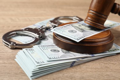 Photo of Judge's gavel, money and handcuffs on wooden table, closeup