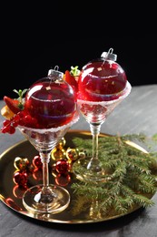 Photo of Creative presentation of Christmas Sangria cocktail in baubles and glasses on grey table against black background, closeup