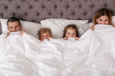 Photo of Couple with children lying under blanket in bed. Happy family
