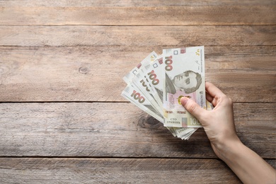 Photo of Woman holding Ukrainian money on wooden background, closeup. Space for text