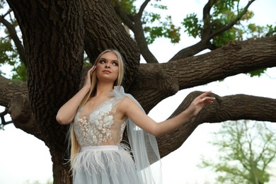 Beautiful girl wearing fairy dress near tall tree outdoors