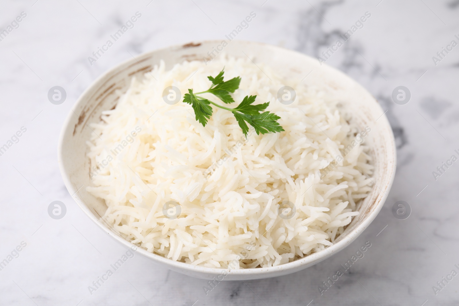 Photo of Bowl of delicious rice with parsley on light table, closeup