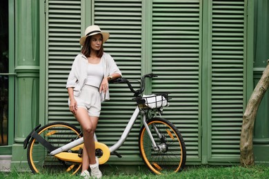 Beautiful young woman with bicycle near green wall outdoors. Space for text