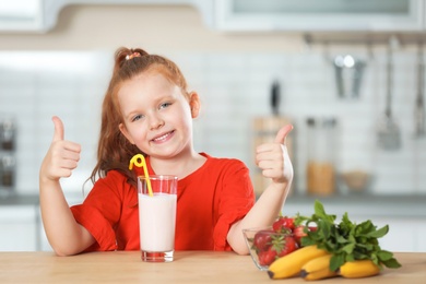 Photo of Little girl with glass of delicious milk shake in kitchen